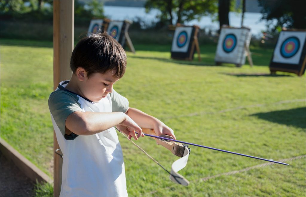 Young kid practising his archery, Mixed race child doing outdoors activity in summer camp adventure.